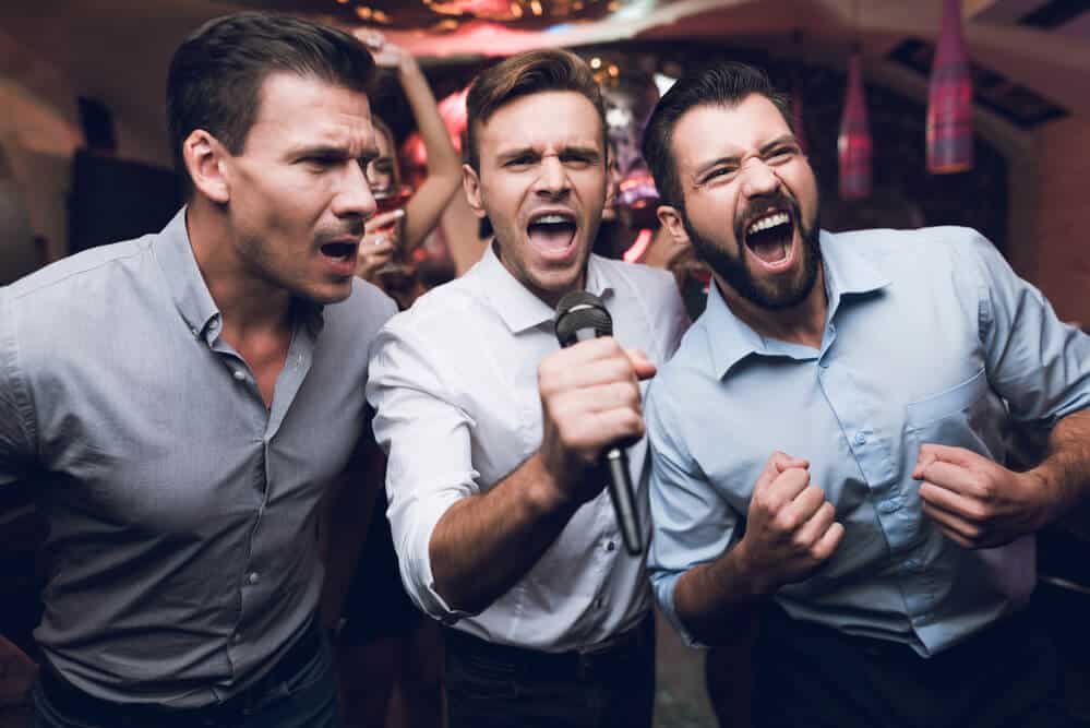 Three men sing at a karaoke club. Young people